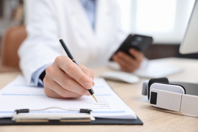 Photo of Doctor with smartphone working at table in clinic, selective focus. Online medical consultation
