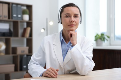 Photo of Doctor in headphones having online consultation at table indoors