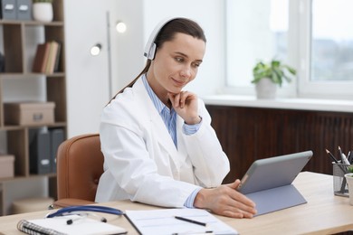 Photo of Doctor in headphones having online consultation via tablet indoors