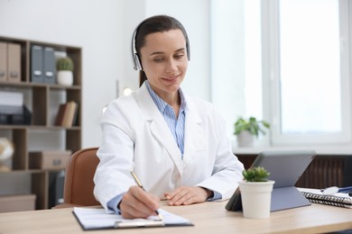 Photo of Doctor in headphones having online consultation via tablet indoors
