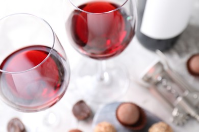 Photo of Red wine in glasses and truffle bonbons on light table, selective focus