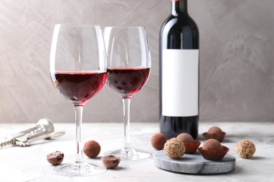 Photo of Red wine and truffle bonbons on white table against grey background, closeup