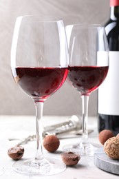 Photo of Red wine and truffle bonbons on white table against grey background, closeup