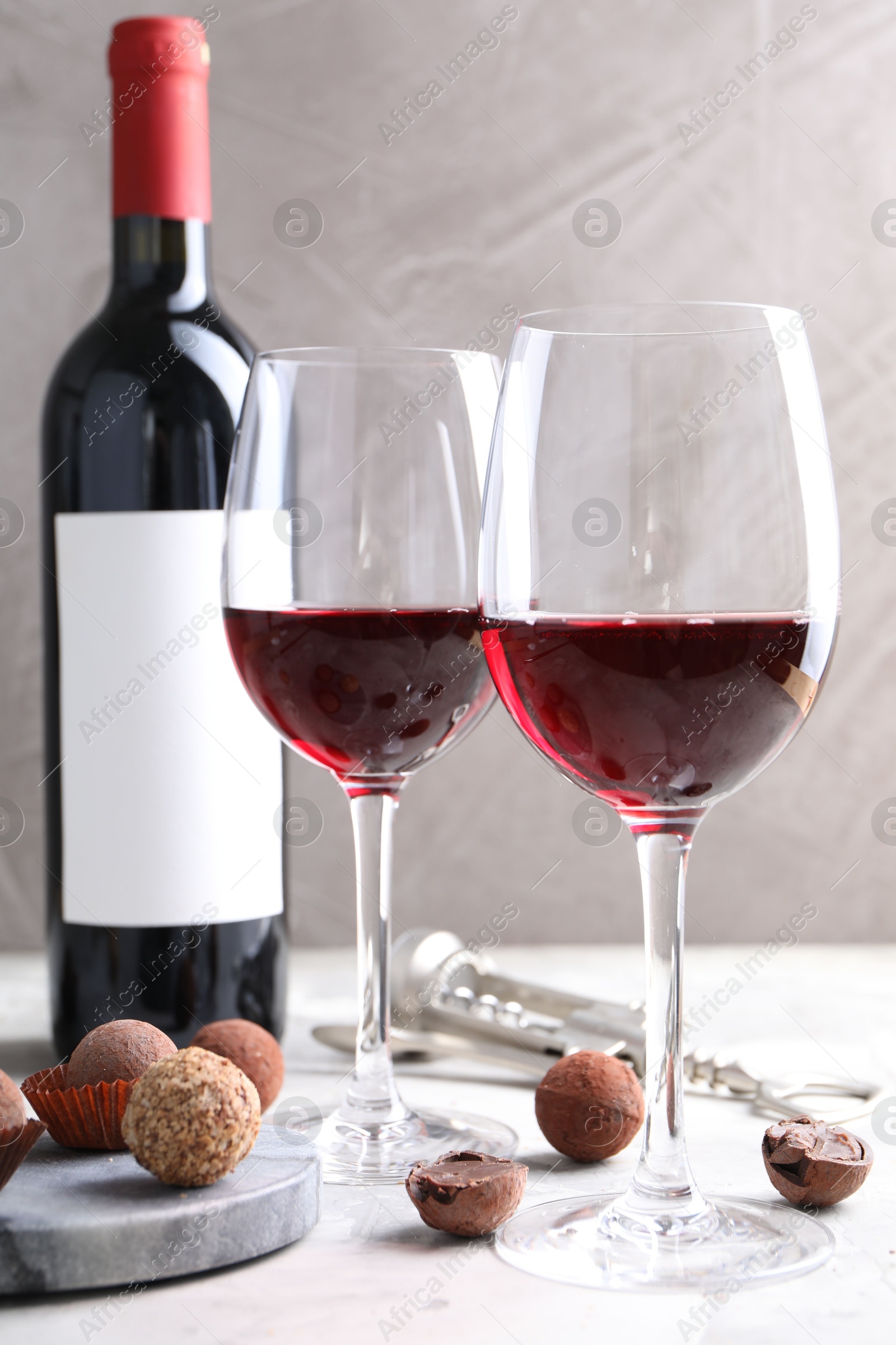 Photo of Red wine and truffle bonbons on white table against grey background, closeup