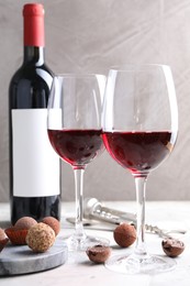 Photo of Red wine and truffle bonbons on white table against grey background, closeup
