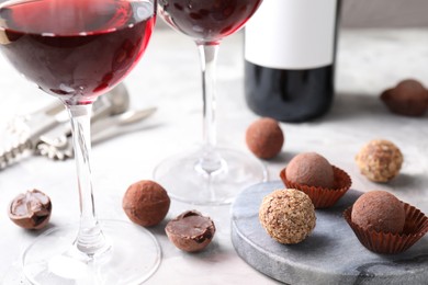 Photo of Red wine and truffle bonbons on white table, closeup
