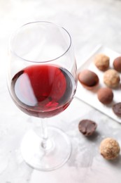 Photo of Red wine in glass and truffle bonbons on light table, selective focus