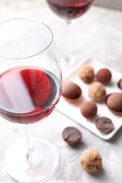 Photo of Red wine in glass and truffle bonbons on light table, selective focus