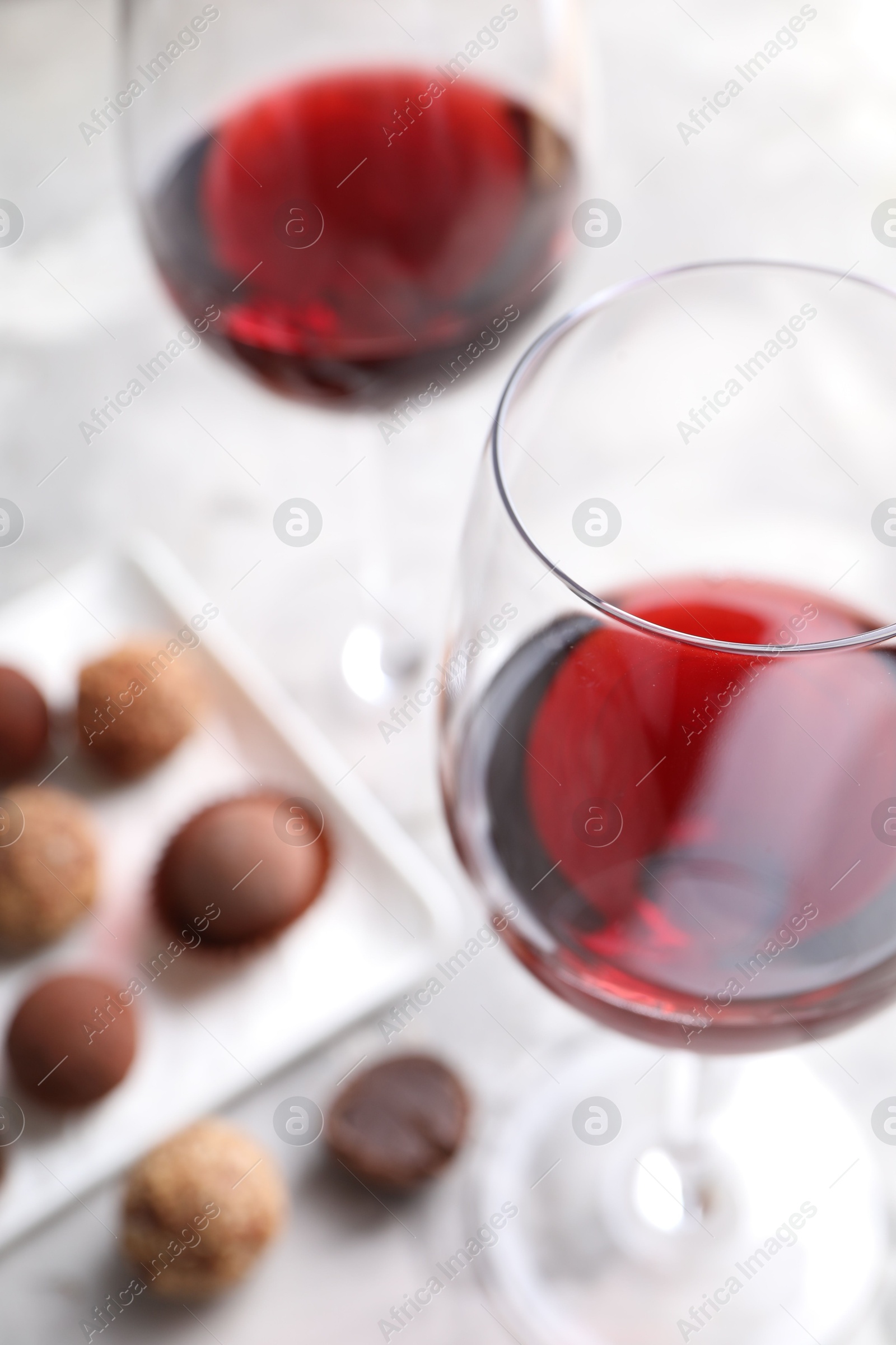 Red wine in glasses and truffle bonbons on light table, selective focus Photo of Red wine in glasses and truffle bonbons on light table, selective focus