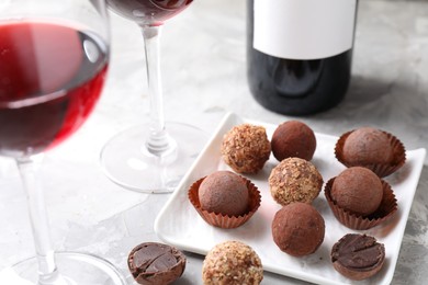 Photo of Red wine in glasses and truffle bonbons on light textured table, closeup