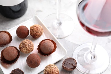 Photo of Red wine in glass and truffle bonbons on light table, closeup