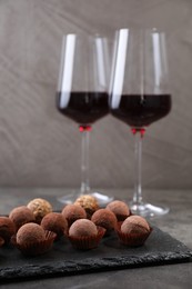 Photo of Tasty truffle bonbons and red wine on grey textured table, closeup