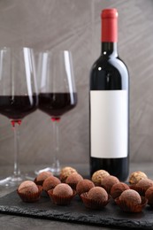 Photo of Tasty truffle bonbons and red wine on grey textured table, closeup