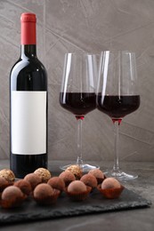 Photo of Tasty truffle bonbons and red wine on grey textured table, closeup