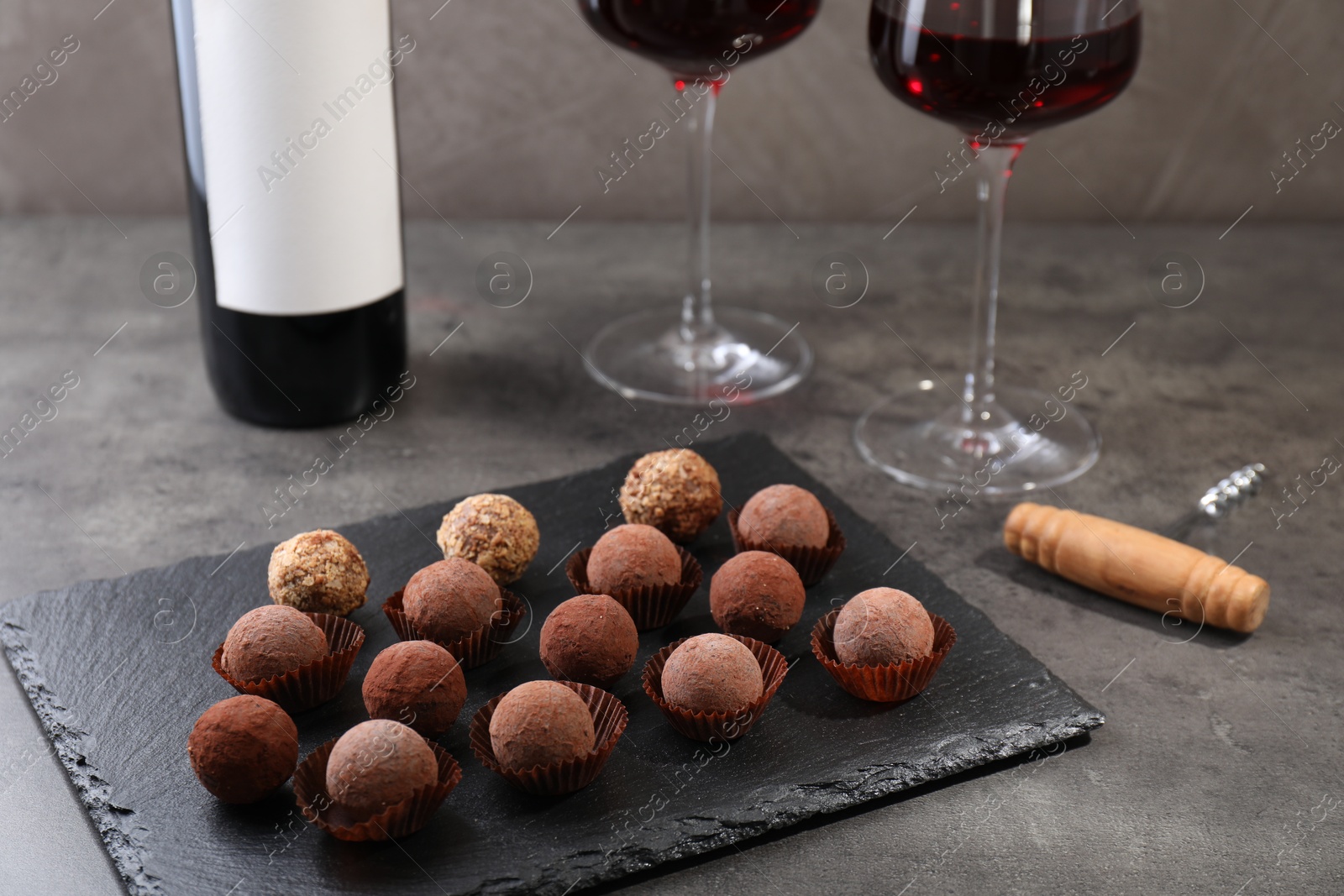 Tasty truffle bonbons, corkscrew and red wine on grey textured table, closeup Photo of Tasty truffle bonbons, corkscrew and red wine on grey textured table, closeup