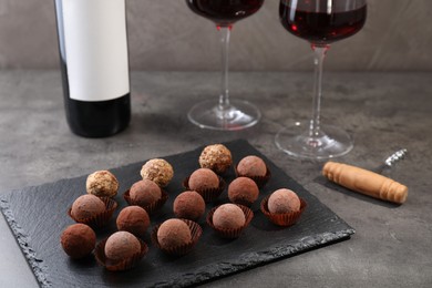Photo of Tasty truffle bonbons, corkscrew and red wine on grey textured table, closeup