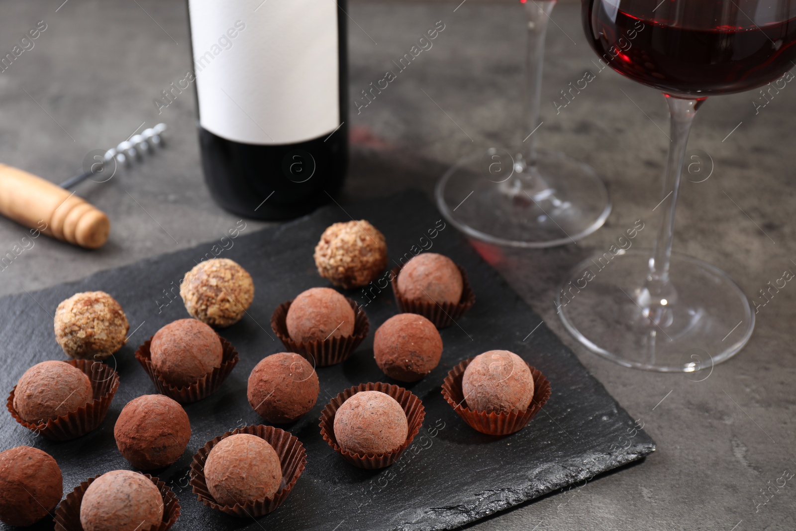 Tasty truffle bonbons, corkscrew and red wine on grey textured table, closeup Photo of Tasty truffle bonbons, corkscrew and red wine on grey textured table, closeup