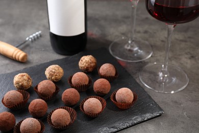 Photo of Tasty truffle bonbons, corkscrew and red wine on grey textured table, closeup