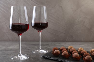 Photo of Tasty truffle bonbons and red wine on grey textured table, closeup