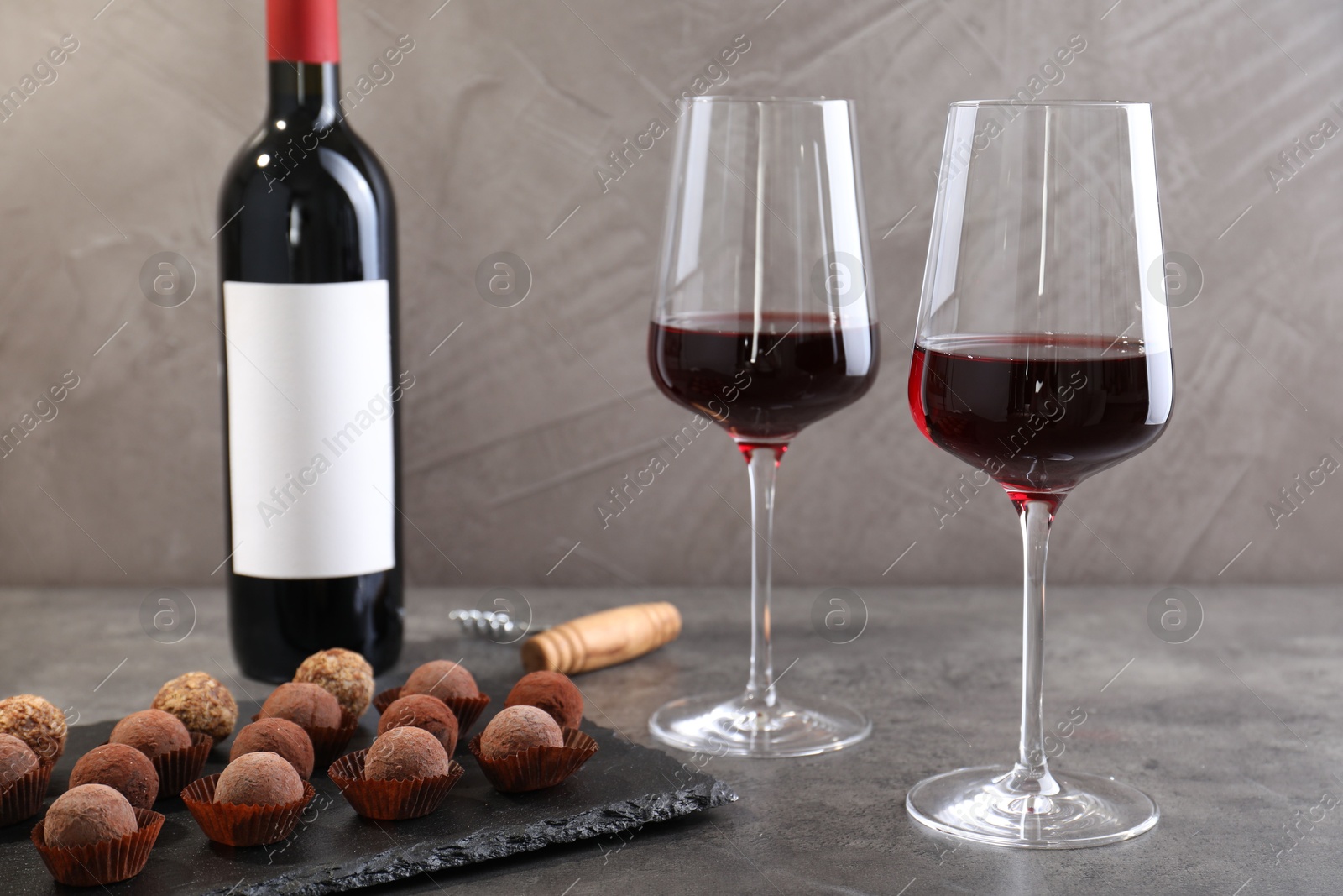Tasty truffle bonbons, corkscrew and red wine on grey textured table, closeup Photo of Tasty truffle bonbons, corkscrew and red wine on grey textured table, closeup