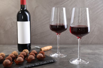 Photo of Tasty truffle bonbons, corkscrew and red wine on grey textured table, closeup