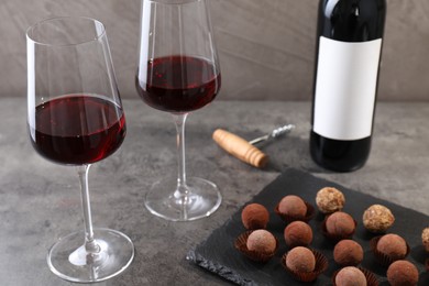 Photo of Tasty truffle bonbons, corkscrew and red wine on grey textured table, closeup
