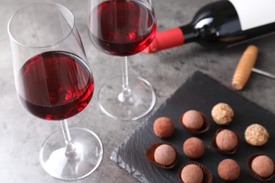 Photo of Tasty truffle bonbons and red wine on grey textured table, closeup