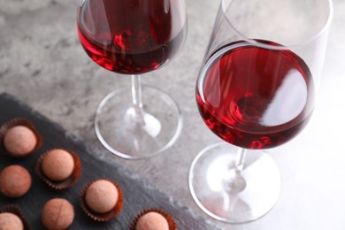 Photo of Red wine in glasses and truffle bonbons on grey textured table, selective focus