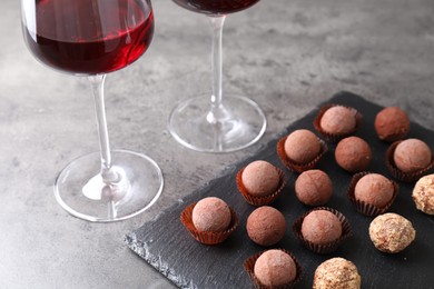 Photo of Tasty truffle bonbons and red wine on grey textured table, closeup