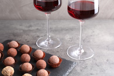 Photo of Tasty truffle bonbons and red wine on grey textured table, closeup