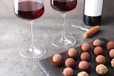 Photo of Tasty truffle bonbons and red wine on grey textured table, closeup