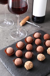 Photo of Tasty truffle bonbons and red wine on grey textured table, closeup