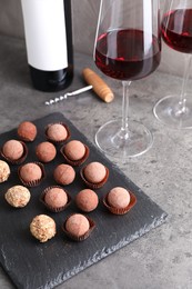 Photo of Tasty truffle bonbons and red wine on grey textured table, closeup