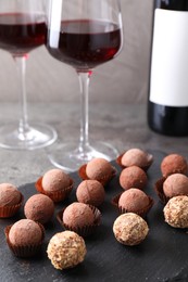 Photo of Tasty truffle bonbons and red wine on grey table, closeup