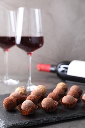 Photo of Tasty truffle bonbons and red wine on grey textured table, closeup