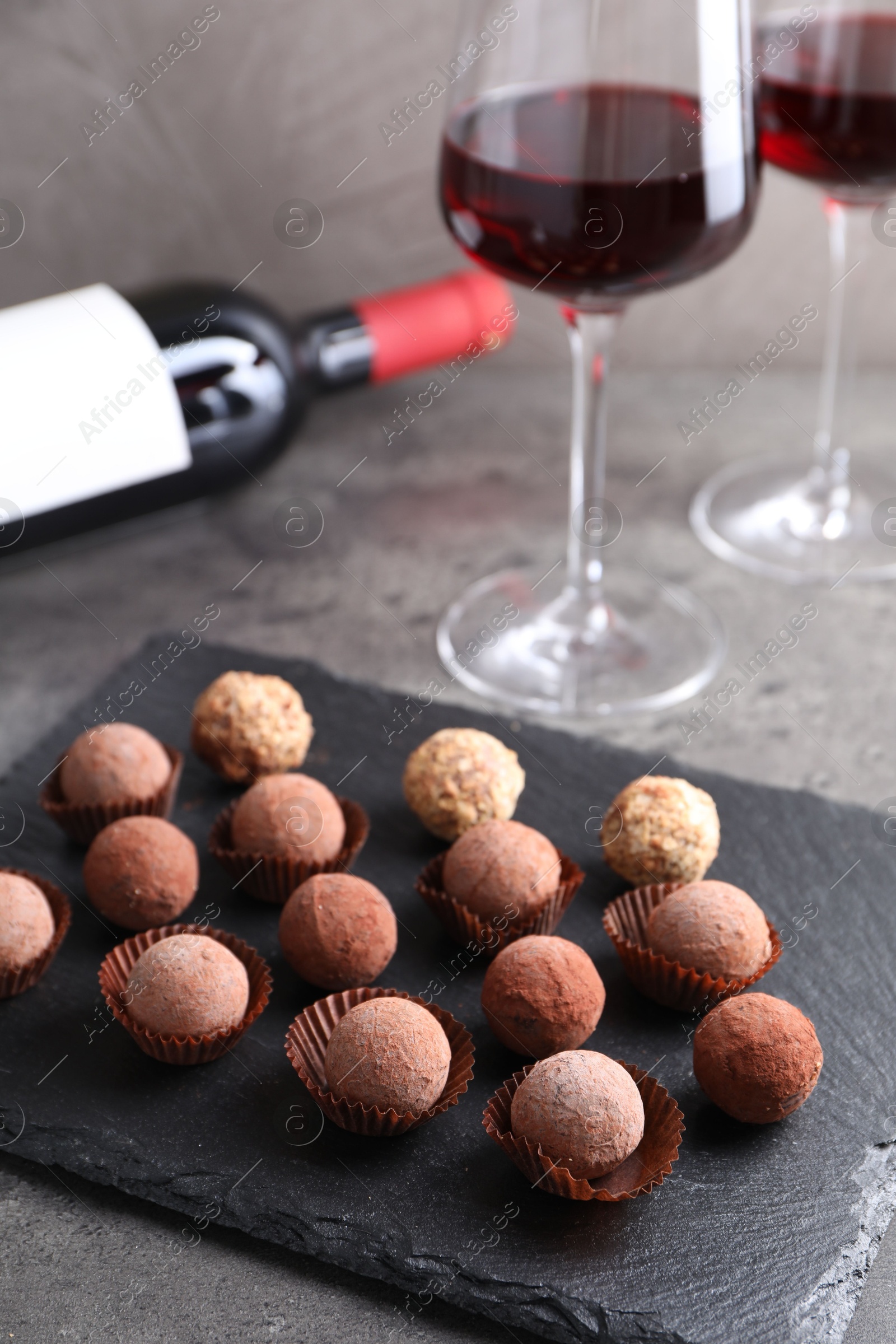 Photo of Tasty truffle bonbons and red wine on grey textured table, closeup