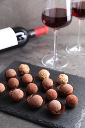 Photo of Tasty truffle bonbons and red wine on grey textured table, closeup