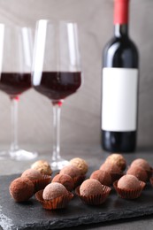 Photo of Tasty truffle bonbons and red wine on grey table, closeup