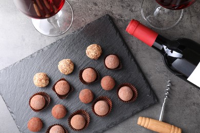 Photo of Tasty truffle bonbons, corkscrew and red wine on grey textured table, flat lay