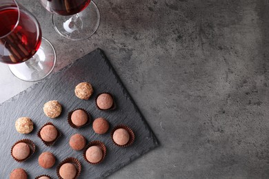 Photo of Tasty truffle bonbons and red wine on grey textured table, flat lay. Space for text