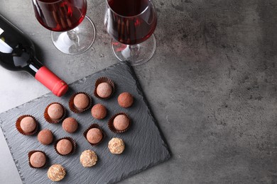 Photo of Tasty truffle bonbons and red wine on grey textured table, flat lay. Space for text