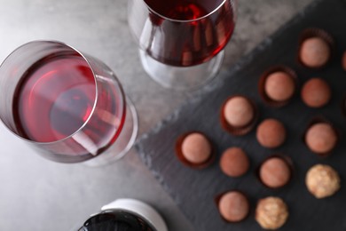Photo of Red wine in glasses and tasty truffle bonbons on grey table, flat lay