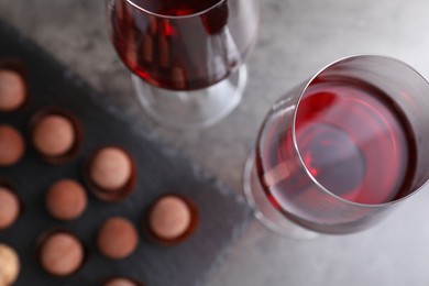 Photo of Red wine in glasses and tasty truffle bonbons on grey table, flat lay