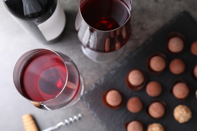 Photo of Red wine in glasses and tasty truffle bonbons on grey table, flat lay