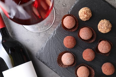 Photo of Tasty truffle bonbons and red wine on grey textured table, flat lay