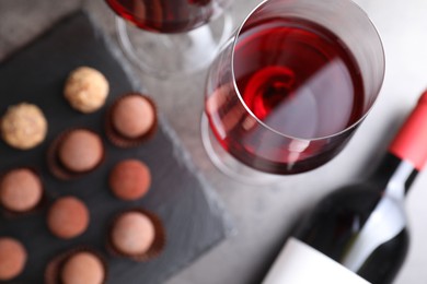 Photo of Red wine in glasses and tasty truffle bonbons on grey table, flat lay