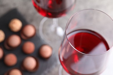 Photo of Red wine in glasses and tasty truffle bonbons on grey table, selective focus