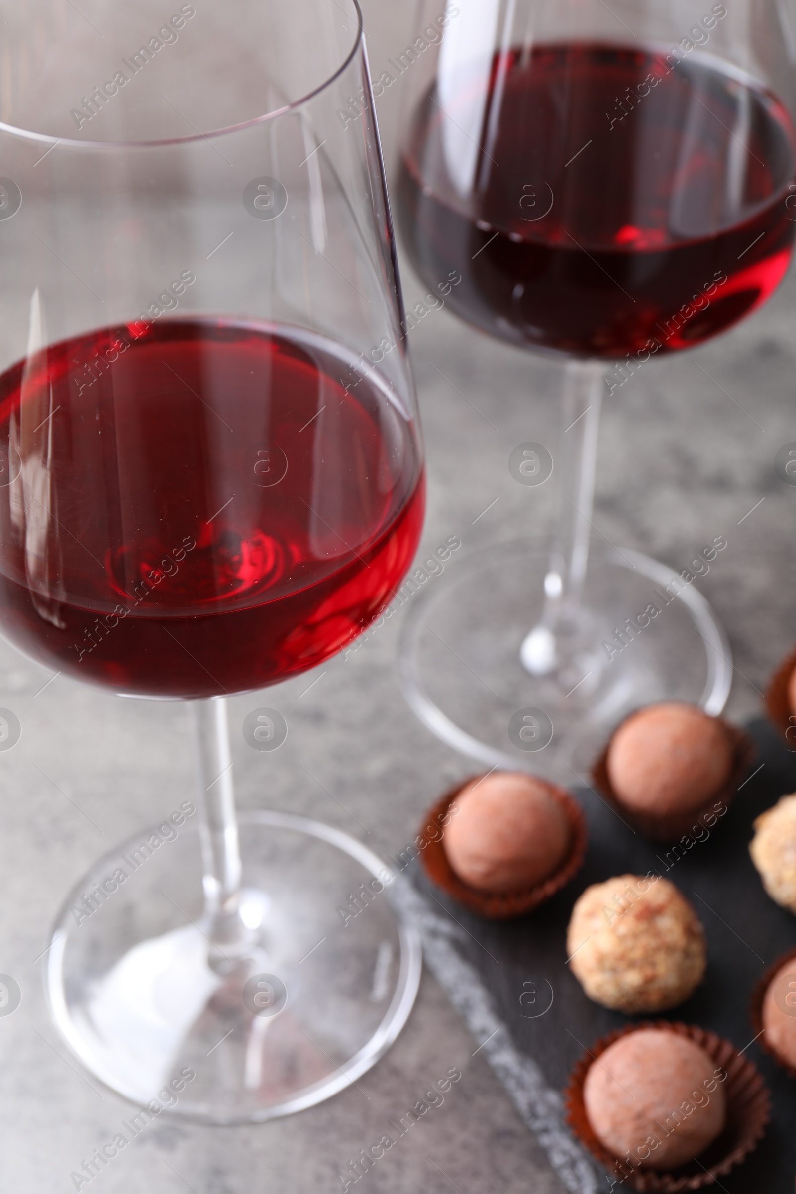 Photo of Tasty truffle bonbons and red wine on grey textured table, closeup