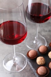 Photo of Tasty truffle bonbons and red wine on grey textured table, closeup
