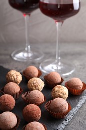 Photo of Tasty truffle bonbons and red wine on grey textured table, closeup